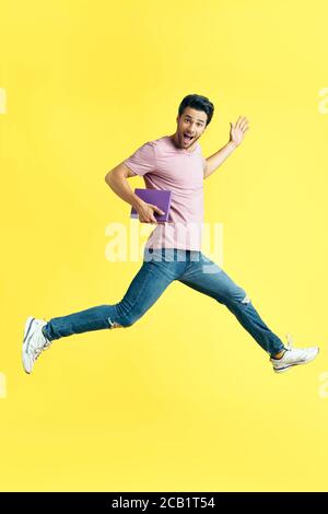 Happy excited man with book jumping on yellow background. carefree and fun concept Stock Photo