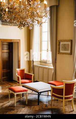 A coffee table with two armchairs and stools in a room with a window and curtains under a chic chandelier. Stock Photo