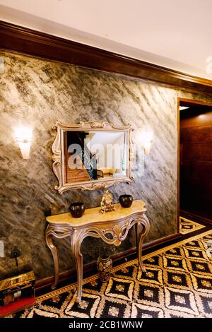 A carved wooden table by the mirror with two lamps on the sides against a brown wall. Stock Photo