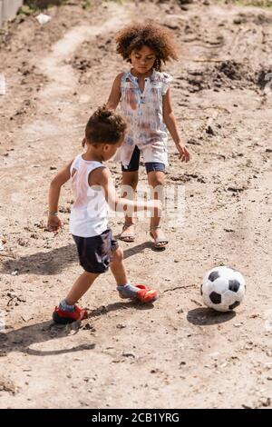 Destitute african american kids playing football on dirty road in slum Stock Photo
