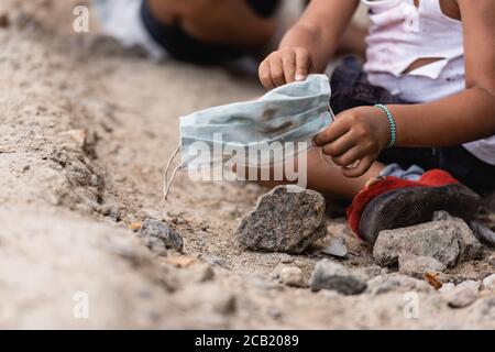 cropped view of poor african american kid holding dirty medical mask Stock Photo