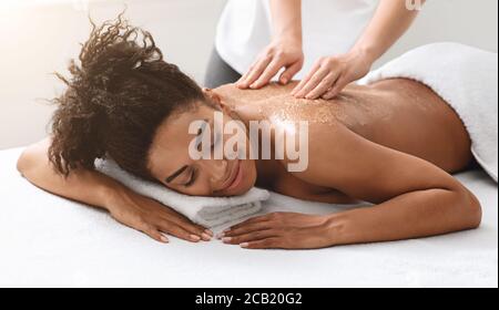 Therapist exfoliating black young woman body at spa Stock Photo