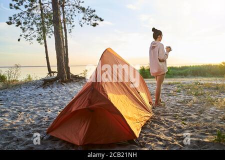 Charming young woman hiker drinking coffee on the beach Stock Photo