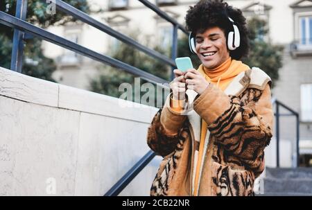 Happy african millennial guy listening music playlist with smartphone app outdoor - Young man having fun with technology trends - Tech, generation z a Stock Photo