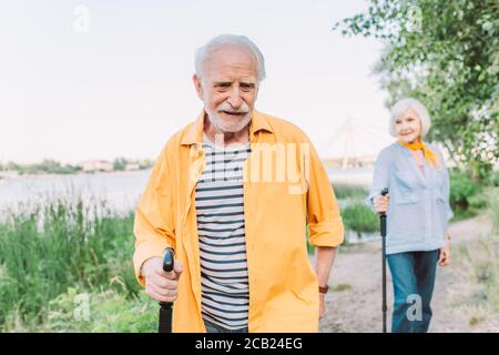 Selective focus of smiling elderly man holding walking stick near wife in park Stock Photo