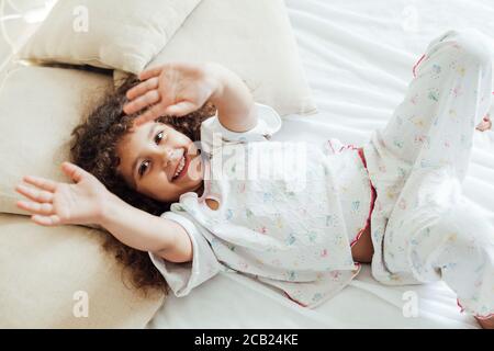 Portrait of a beautiful little curly girl in the morning in the bedroom on the bed Stock Photo