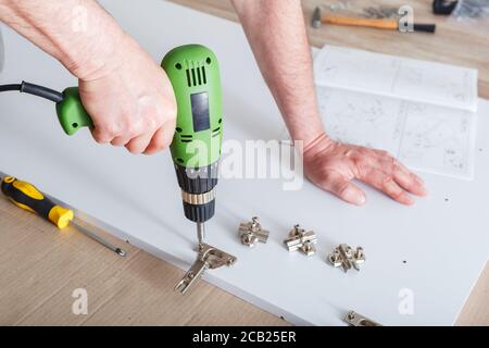 Furniture assembly using drill. Male hands master collects furniture using tools instrument drill in house. Moving, home improvement, furniture repair Stock Photo