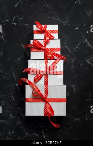 Abstract cake made from gift boxes with a red ribbon on a black stone background. Top view, flat lay. Creative layout
