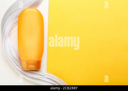 Shampoo bottle mockup strand on lock curl of blonde hair on orange color background. Orange bottle shampoo. Top view copy space.Hair care cosmetics Stock Photo