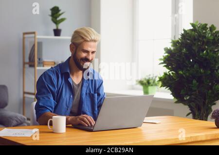 Happy remote worker typing on laptop at table at home Stock Photo