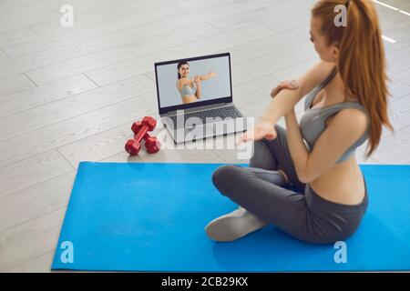 Online fitness concept. Young woman on the floor doing exercises, stretching and uses a video fitness lesson. Stock Photo