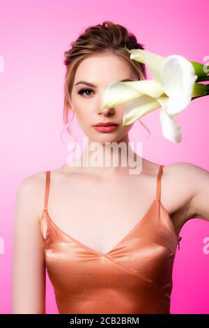 elegant beautiful blonde woman holding calla flowers in front of face isolated on pink Stock Photo