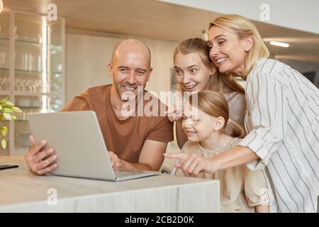 Warm-toned portrait of happy modern family using laptop together while speaking by video chat with relatives in cozy home interior, copy space Stock Photo