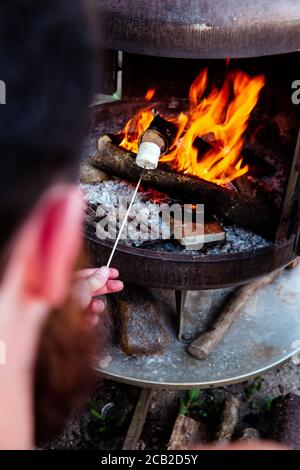 Person roasting over fire flames a marshmallows over campfire at night on a summer day, for smores or snack Stock Photo