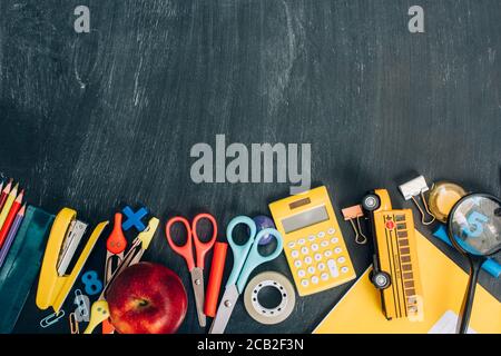 top view of school bus model, ripe apple and school supplies on black chalkboard with copy space Stock Photo