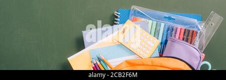 top view of backpack full of school stationery on green chalkboard, horizontal image Stock Photo