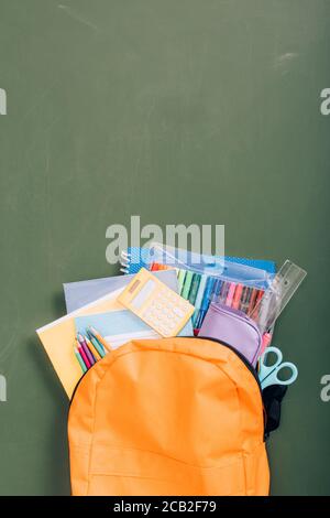 top view of backpack packed with school stationery on green chalkboard Stock Photo