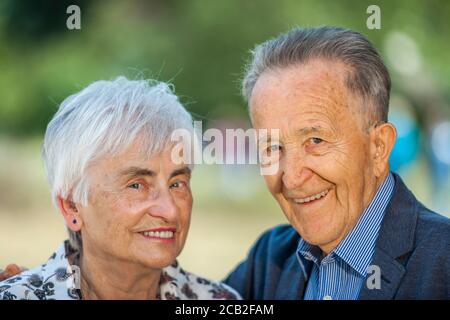 Head-and-shoulder portrait of an 80 year old retired couple in front of a blurred green background looking friendly into the camera. Stock Photo