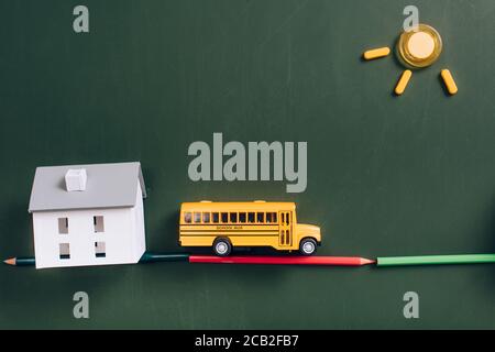 top view of yellow school bus on road made of color pencils, house model and sun made of magnets on green chalkboard Stock Photo