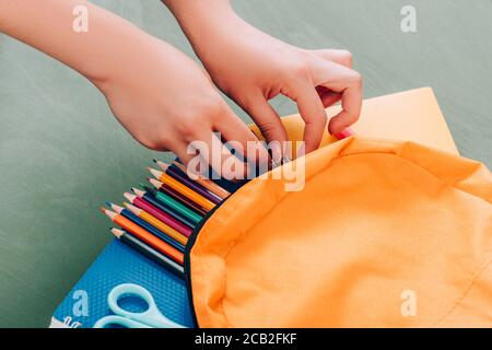 cropped view of student taking stationery from backpack with notebooks, color pencils and scissors on green surface Stock Photo