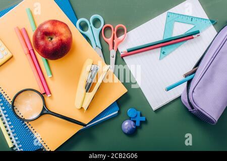 top view of whole apple and notebooks near school stationery on green chalkboard Stock Photo