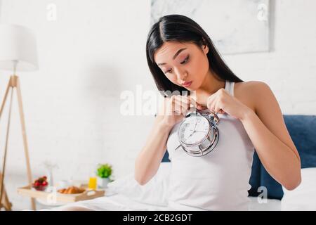 Surprised asian woman looking at alarm clock in bedroom at morning Stock Photo