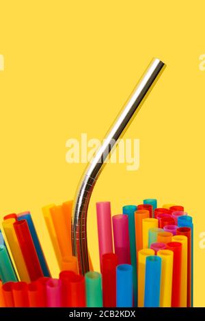 a reusable stainless steel drinking straw standing out from some disposable plastic drinking straws of different colors, on a yellow background Stock Photo