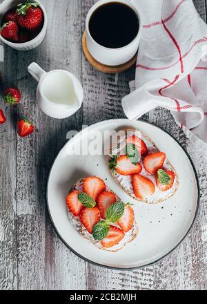Two toasts with strawberry, mint, cup of coffee on wooden table ...