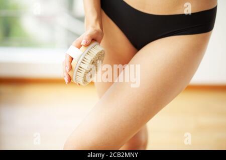 Woman arm holding dry brush to top of her leg, cellulite treatment and dry brushing. Stock Photo