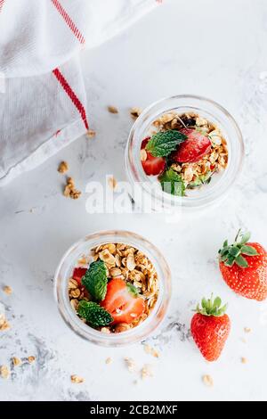 Two jars with tasty parfaits made of granola, strawberries and yogurt on white marble table, top view Stock Photo