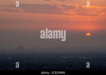 Sun setting over Manchester city on a dusty summer evening. The poor air visibility and clouds helped produce a spectacular deep orange red sunset. UK Stock Photo