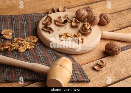 High angle shot of walnuts and crushed shells on a cutting board next to a small wooden hammer Stock Photo