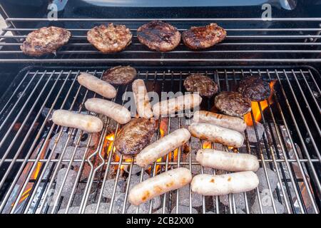 Sausage and beef burgers cooking on a barbecue. Stock Photo