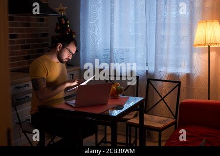 young hardworking man of caucasian appearance, with beard work on laptop at home, holding documents in hands Stock Photo