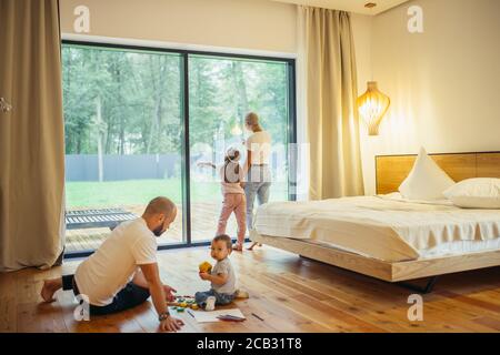 Young parents with their children in room. Mother and daughter, father with son playing on floor. Growing generation, family concept Stock Photo