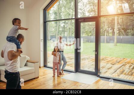 Parents with children look at panoramic window together, relaxing together, spending time at home. Modern house interior Stock Photo