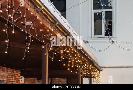 Christmas decoration of buildings, garlands with light bulbs on the facade and roof of the street market against the dark night sky, winter holiday se Stock Photo
