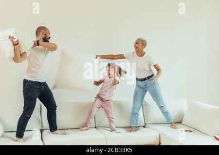 Happy family fighting with pillows on bed. Jumping and having fun children and parents. Happy family concept. White colors Stock Photo