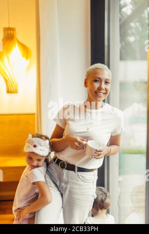 Cute girl hugging glad mother. Young, beautiful mom and daughter smiling. Mother look at camera. Cheerful, joyful child and mom posing in light room w Stock Photo