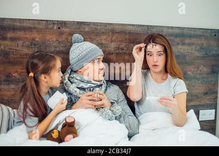 caucasian woman stay in shock after looking at thermometer, man and daughter lying on bed near her Stock Photo