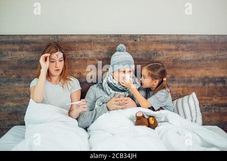ill caucasian family lying on bed together, suffering from disease. Unhealthy man, woman and child girl treating at home Stock Photo