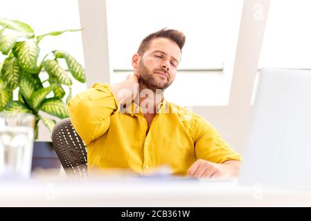 Shot of a businessman experiencing stress during sitting behind his laptop and suffering from strong head pain. Stock Photo