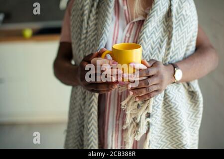 Diverse love couple, close up. Focus on woman s hands with yellow mug, covered by mans hands Stock Photo
