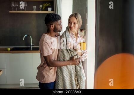 Multi-ethnic relationships concept. African young man looking at his white-skin woman with loving and caring expression, covering her with a warm blan Stock Photo