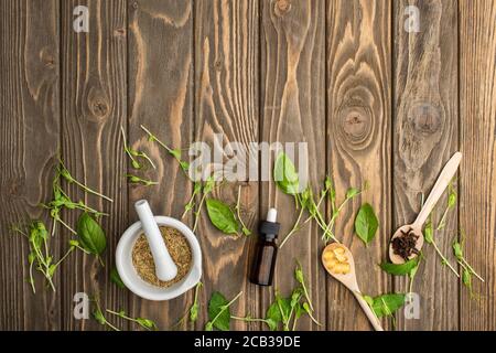 top view of pills in spoons, mortar, green herbs and bottle on wooden surface, naturopathy concept Stock Photo