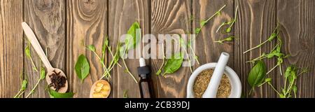 top view of pills in spoons, mortar, green herbs and bottle on wooden surface, naturopathy concept Stock Photo