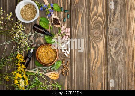 top view of pills in spoons, green herbs and wildflowers on wooden surface, naturopathy concept Stock Photo