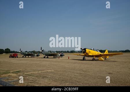 Two parked Spitfire aircraft and a T6 Harvard on Headcorn grass Aerodrome in Kent, South East England, UK Stock Photo