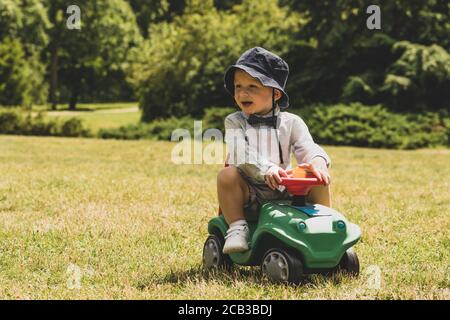 Child playing on green car on green meadow with copy space during sunny summer day Stock Photo