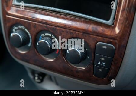 The central control console on a brown decorated panel inside the car close-up with buttons and climate control toggle switches. Stock Photo